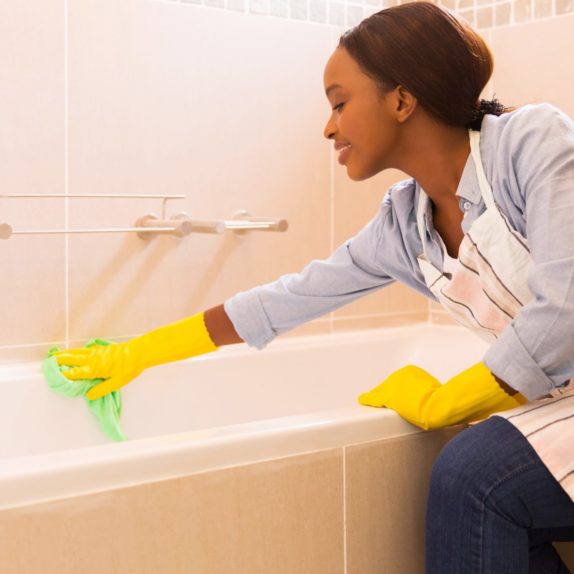 young african housewife cleaning up bathtub at home